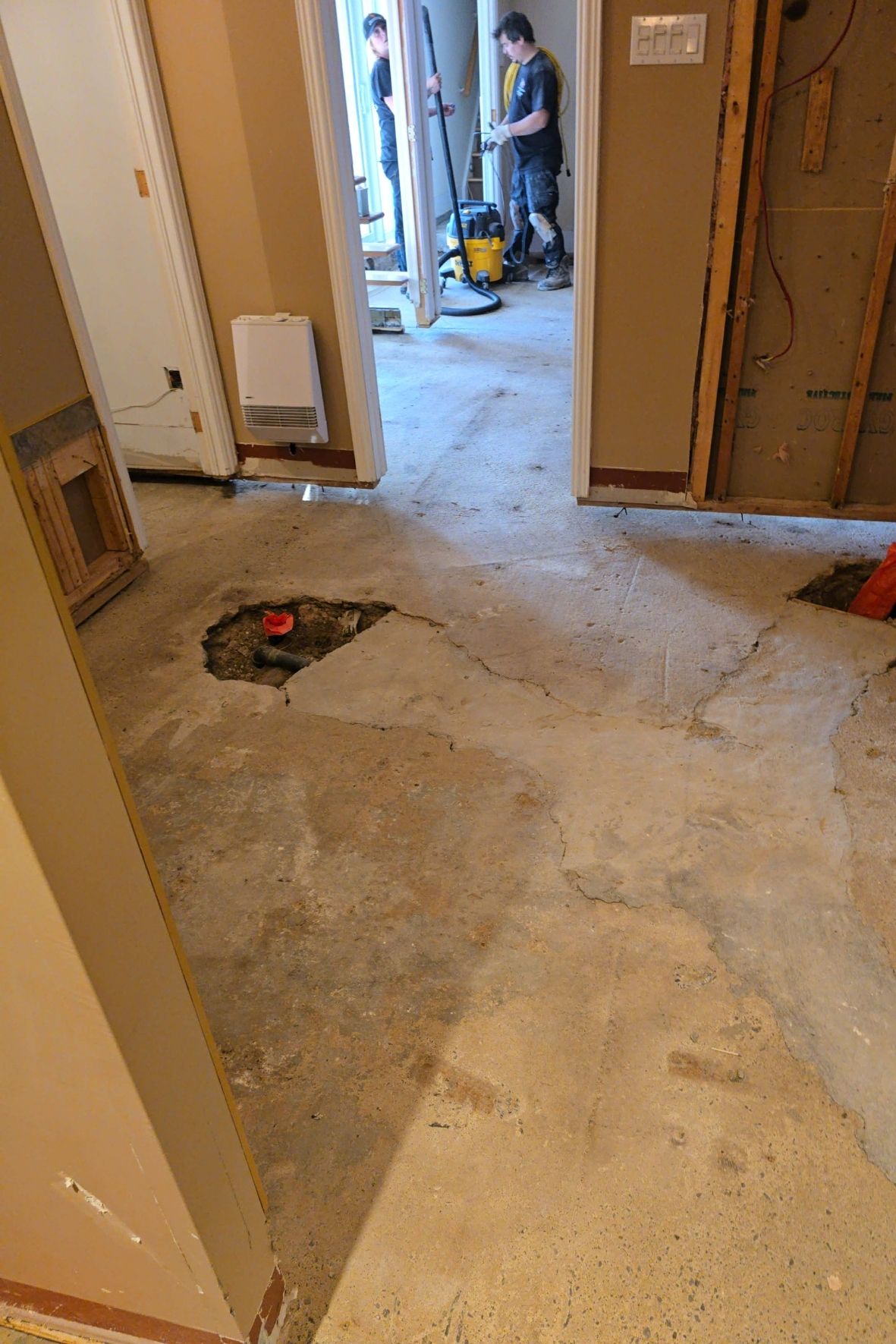 Plancher de sous-sol ouvert avec sections retirées et travailleurs en arrière-plan dans un bâtiment en rénovation  sur la Rive-Nord de Montréal